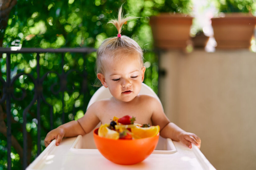 toddler-sits-high-chair-balcony-looks-bowl-fruit-1024x683.jpg